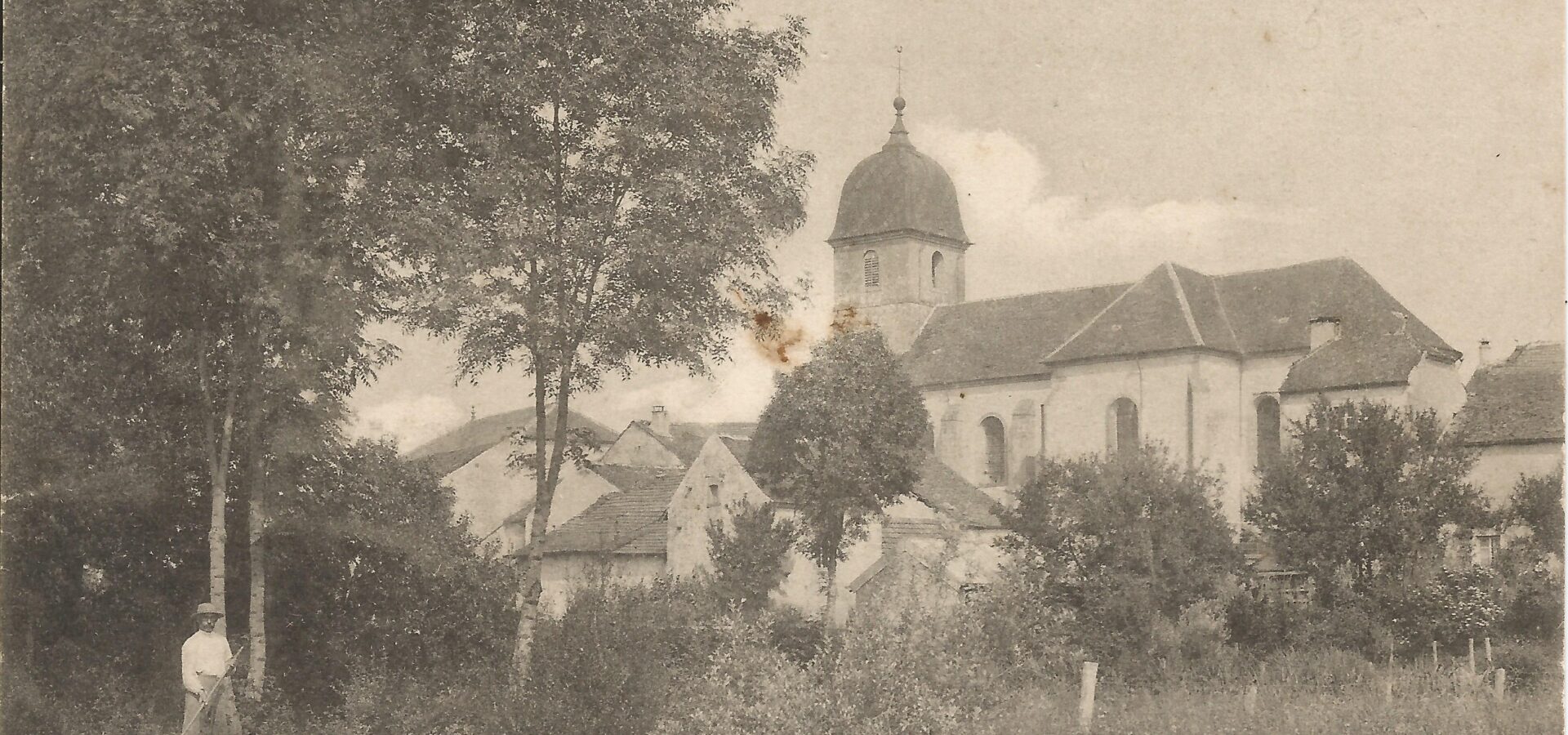 Carte postale de 1917 représentant un panorama de l'église de Villers-lès-Luxeuil ainsi qu'un paysan faisant les foins